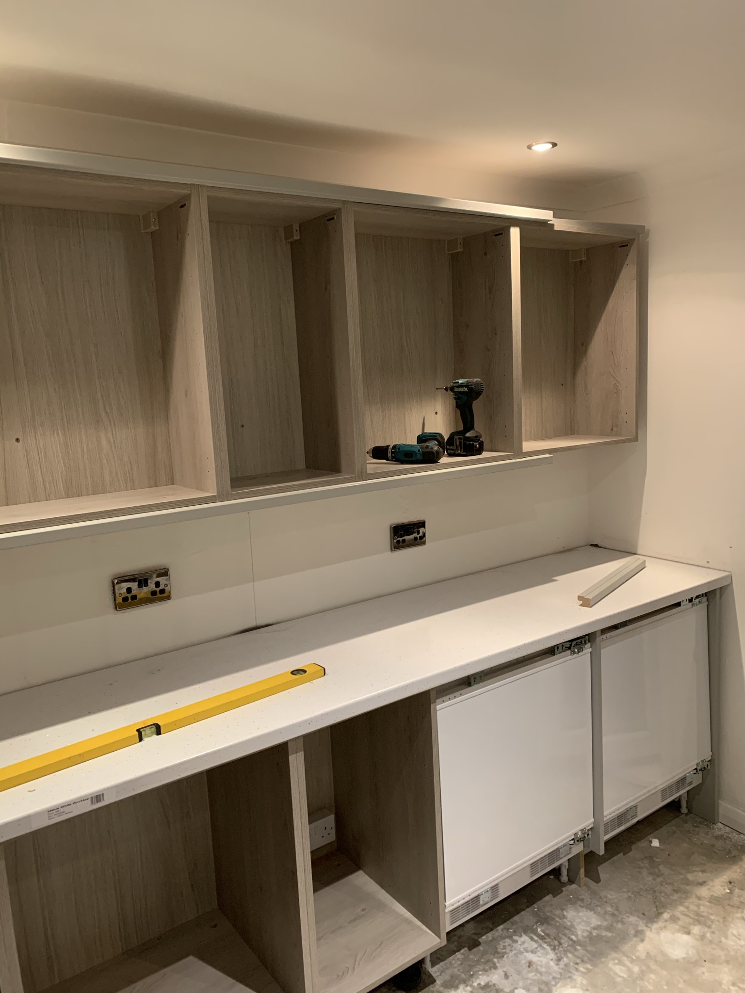 Wood-effect kitchen units being fitted, spirit level on the worktop
