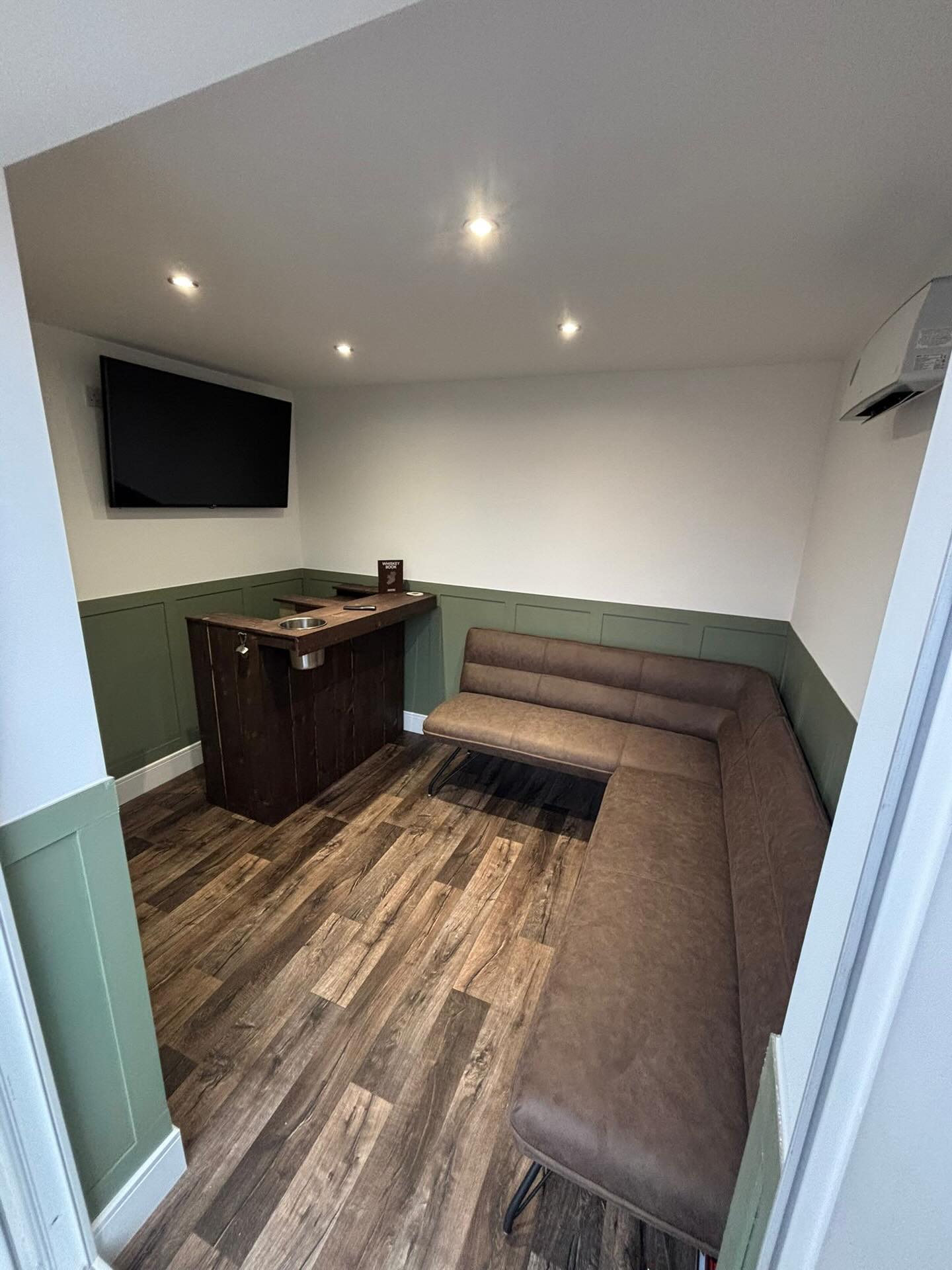 Room fitted out with half-height green panelling, a bar counter and a wall-mounted TV